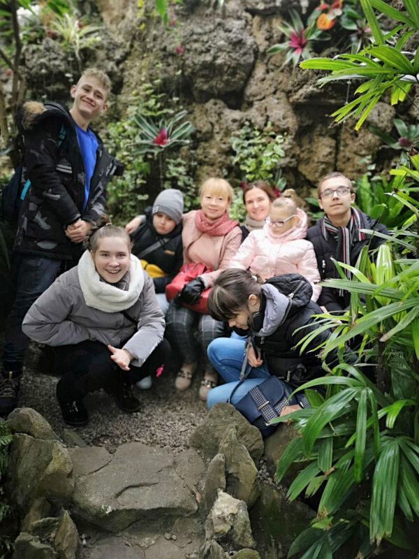 Zdjęcie przedstawia grupę uczniów i dwie nauczycielki. Wszyscy uśmiechają się. W tle skała z roślinnością.